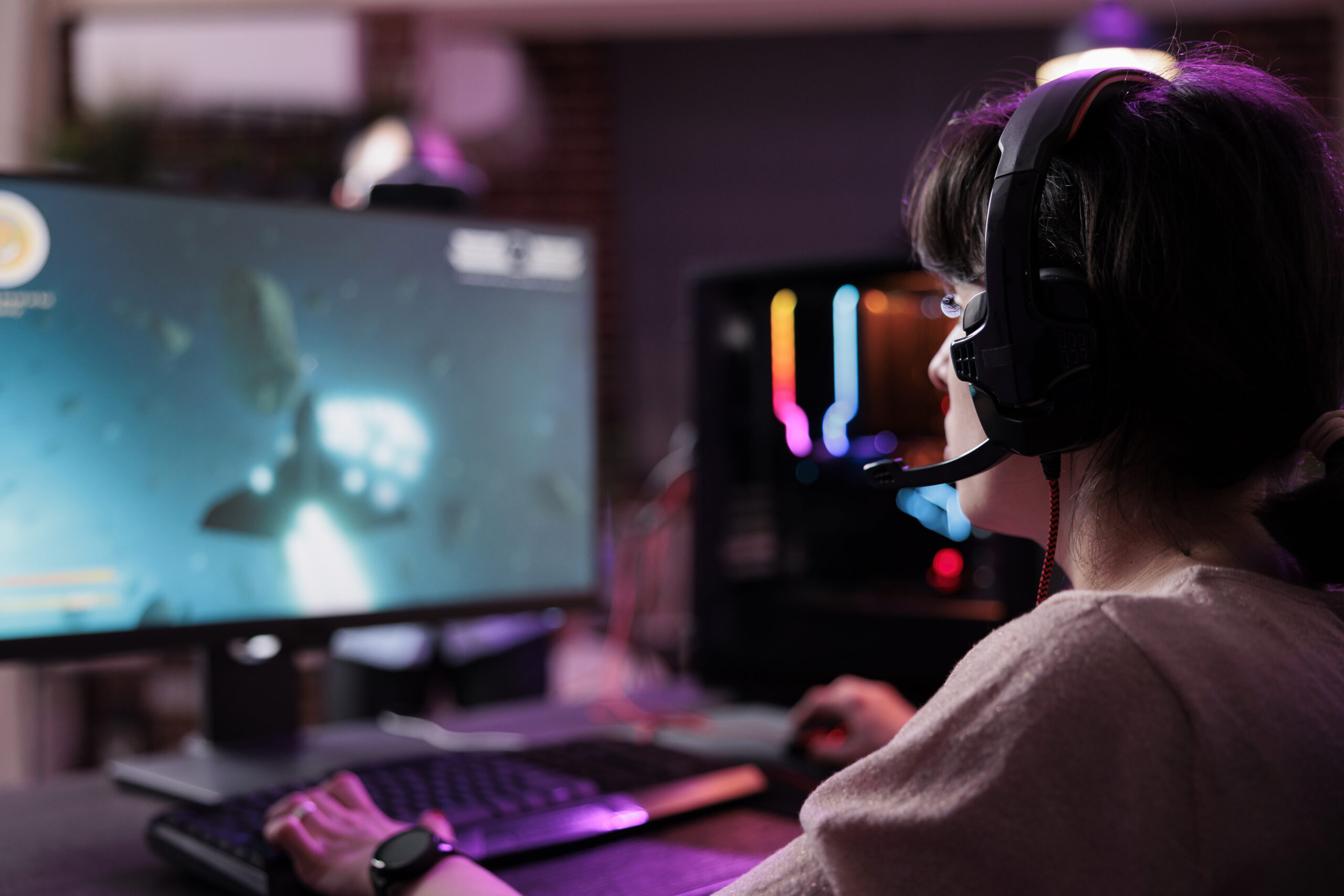 Young streamer playing video games online on live stream, using computer and neon lights in living room. Female gamer having fun with action gameplay on virtual shooting tournament.